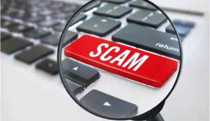 A magnifying glass focusing on a red 'SCAM' button on a keyboard, highlighting the theme of internet deception and security awareness.